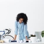 Femme au bureau debout regardant ses plans sur la tête penchée vers le bas